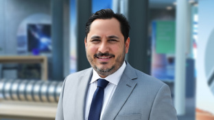 Yosafat Esquitin, Business Development Manager, standing against a plain light background wearing a patterned button-up shirt.